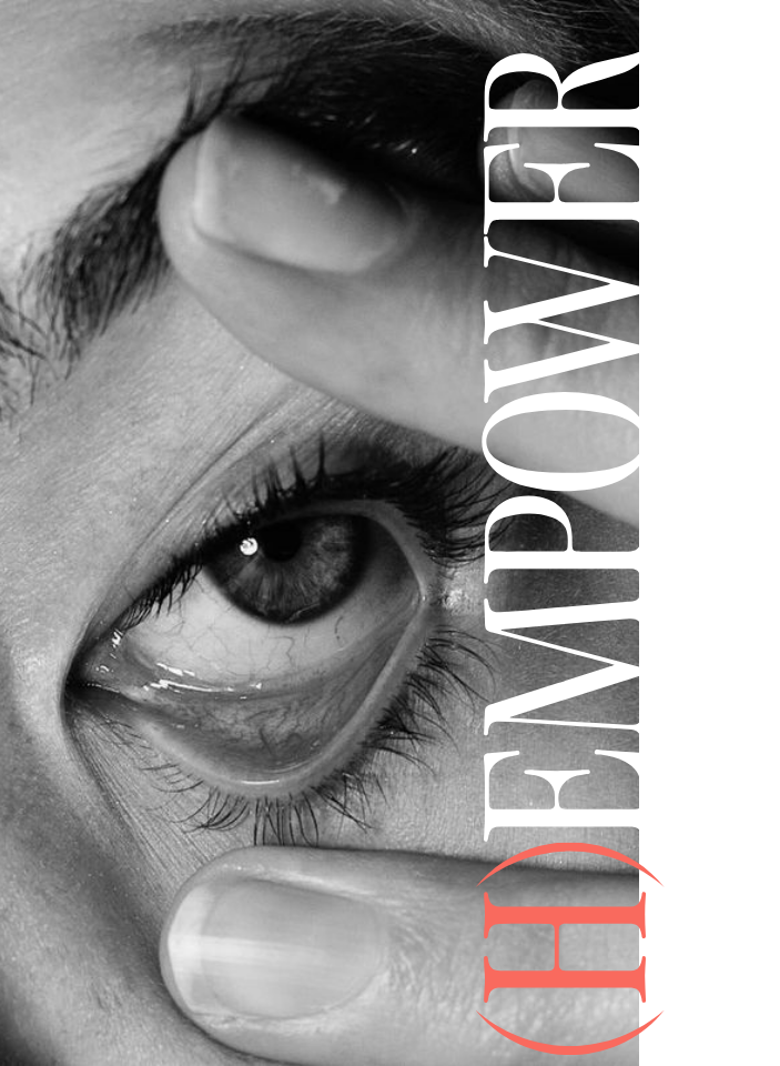 Un primer plano en blanco y negro del ojo de una persona, con los dedos tirando suavemente del párpado para abrirlo. La palabra EMPOWER aparece superpuesta verticalmente en texto blanco de gran tamaño, con (H) en rojo en la parte inferior.