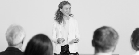 mujer de negocios dando una conferencia photoaidcom greyscale 450x180